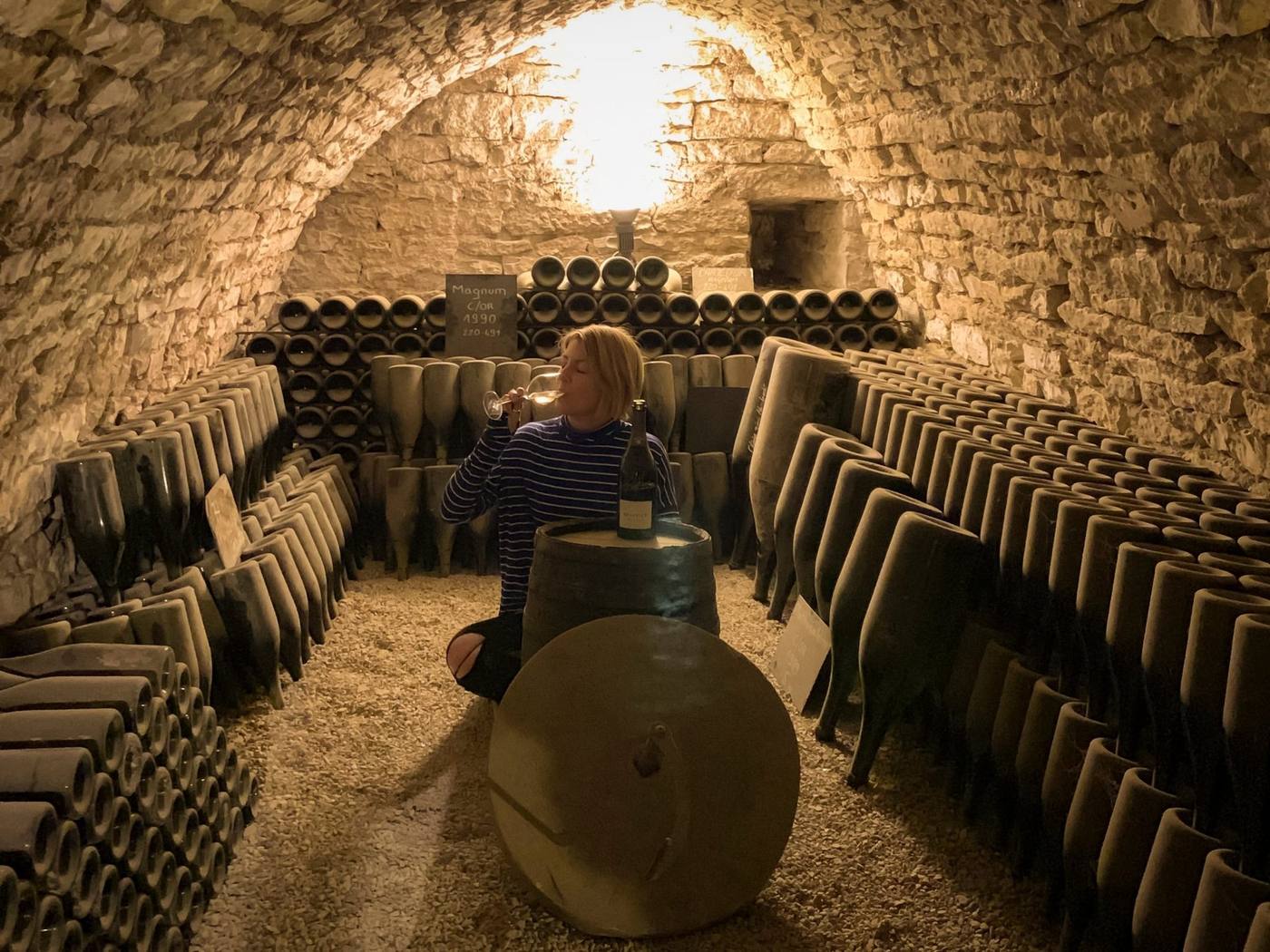 Kendal Montgomery sipping Champagne in a vaulted stone cellar lined with aging bottles