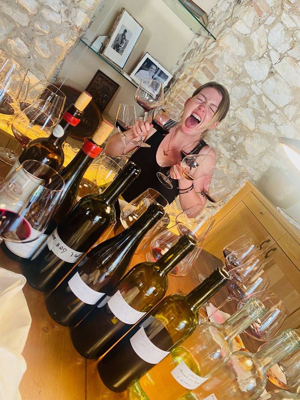 Kendal Montgomery laughing with an armful of wine glasses behind a table crowded with bottles and glasses