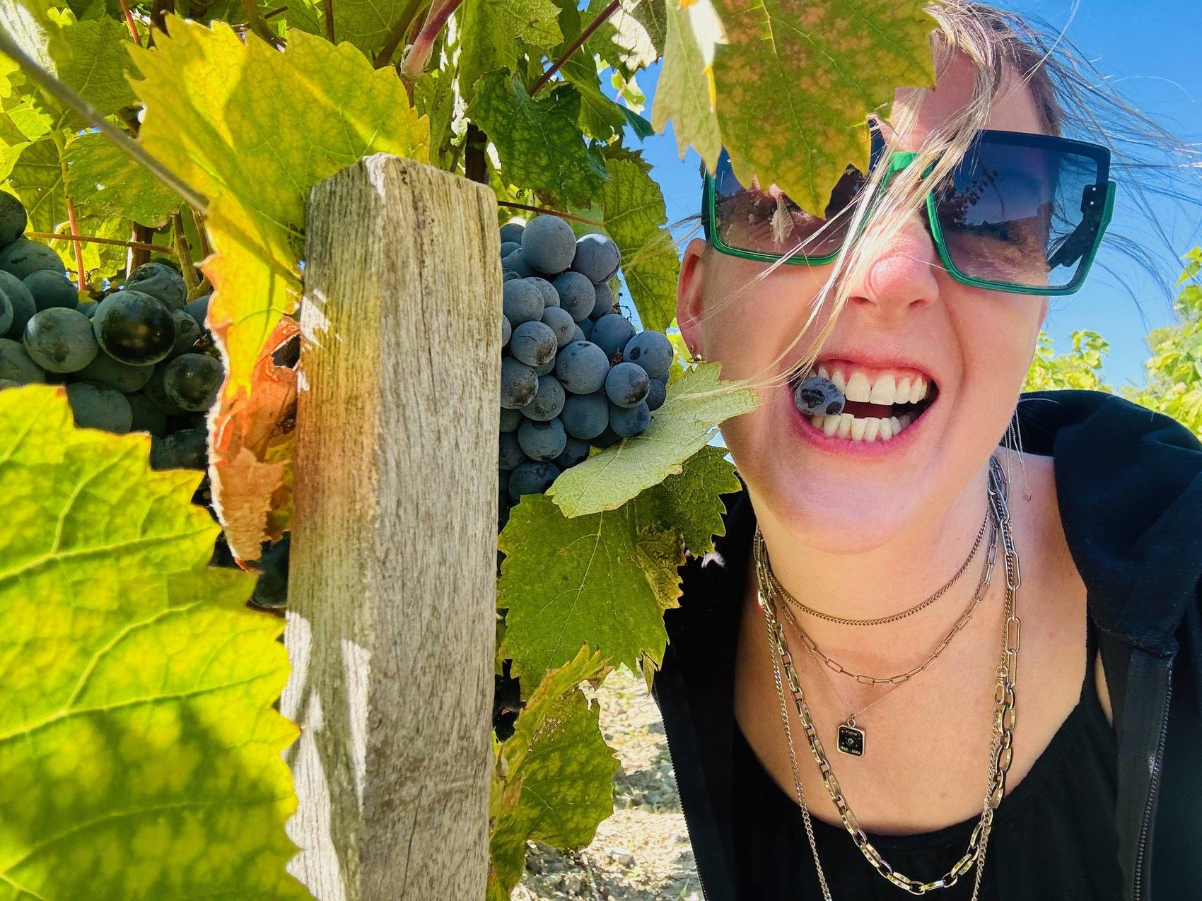 Kendal Montgomery grinning in a vineyard with a grape between her teeth