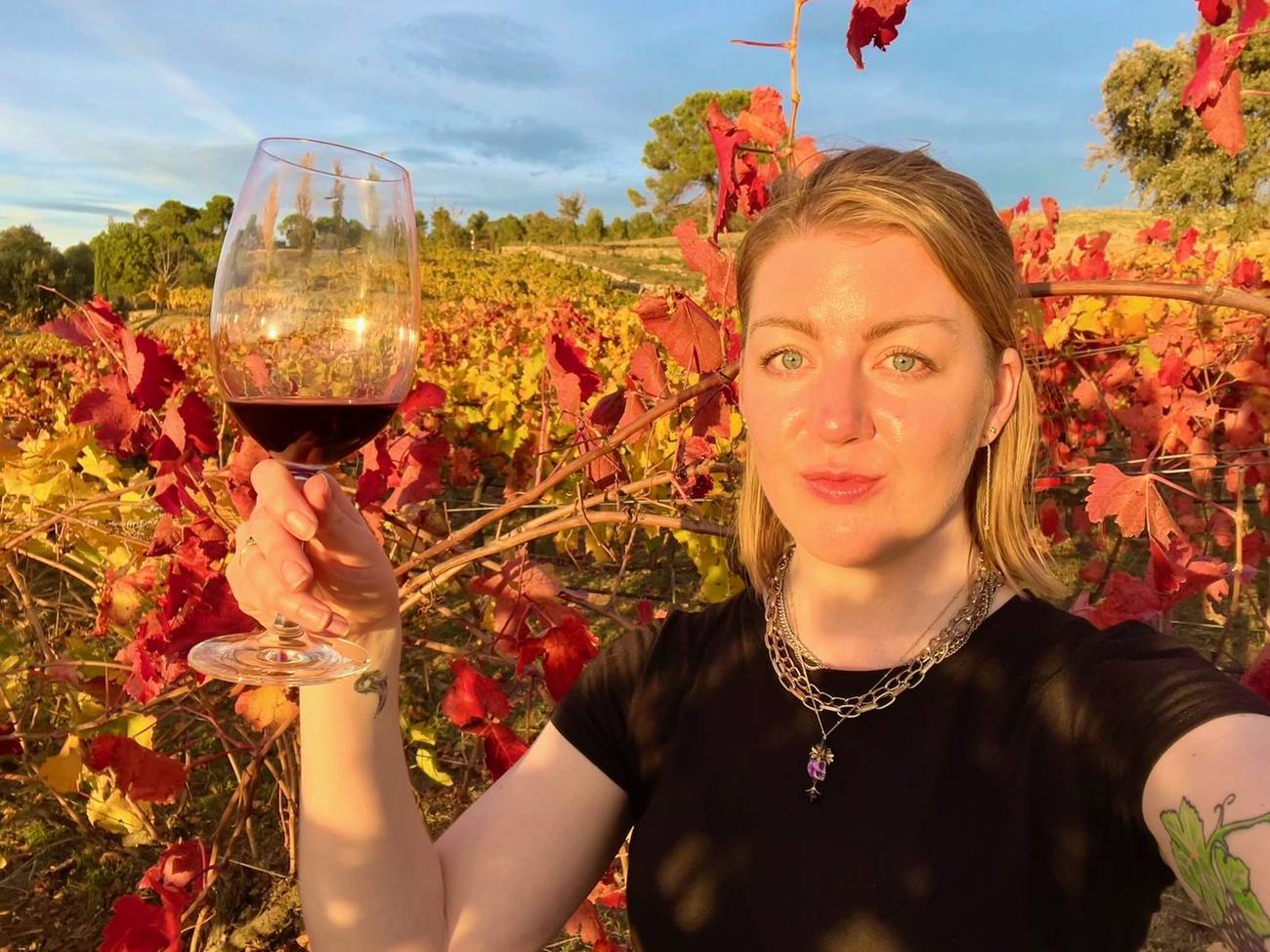 Kendal Montgomery raising a glass of red wine among autumn-red vines